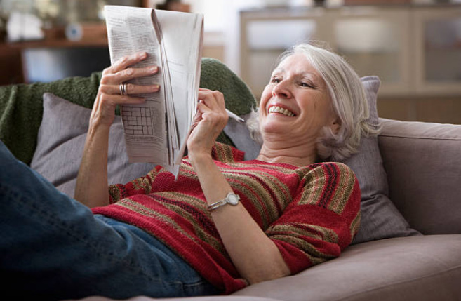 mujer en sillón con periódico y pasatiempos